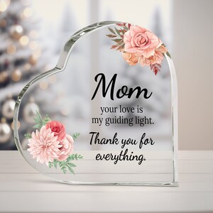 May include: A clear glass heart-shaped paperweight with pink and white floral designs and the text "Mom your love is my guiding light. Thank you for everything."