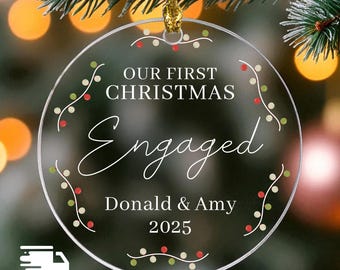 May include: Clear, round Christmas ornament with the text "OUR FIRST CHRISTMAS Engaged Donald & Amy 2025". The ornament is decorated with a string of lights in red, green, and white. A gold string is attached for hanging.