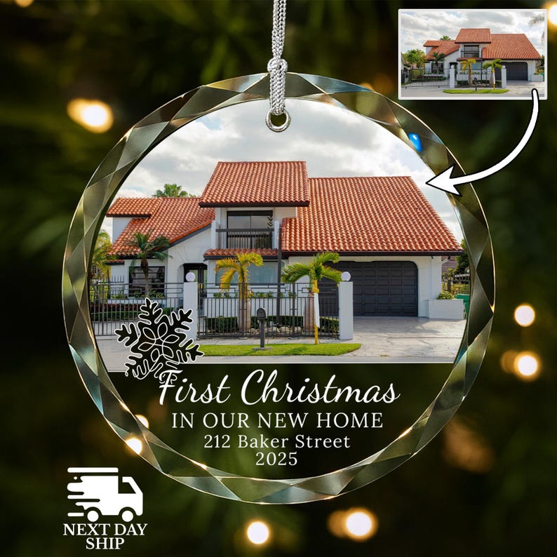 May include: A clear, faceted glass Christmas ornament with a silver string. The ornament features a house with a red tile roof and the text "First Christmas in Our New Home, 212 Baker Street, 2025."
