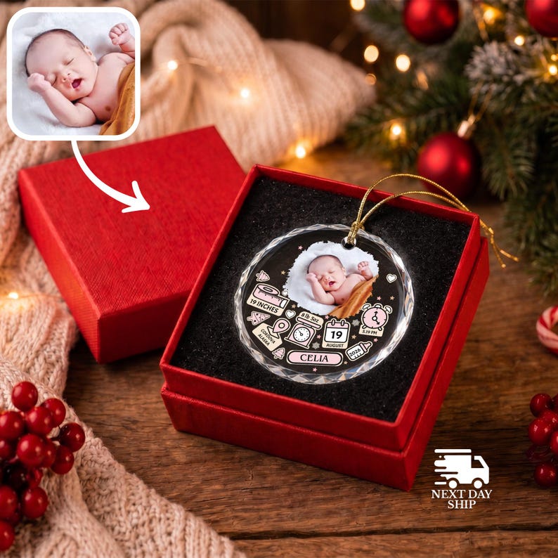 K&ouml;nnte beinhalten: Ein rundes, klares Glasornament mit einem Foto eines Neugeborenen und aufgedruckten Geburtsdaten, darunter der Name Celia, 48,26 cm, 2863 Gramm, 19. August und Cordova Alaska, pr&auml;sentiert in einer roten Geschenkbox mit goldener Aufh&auml;ngung.