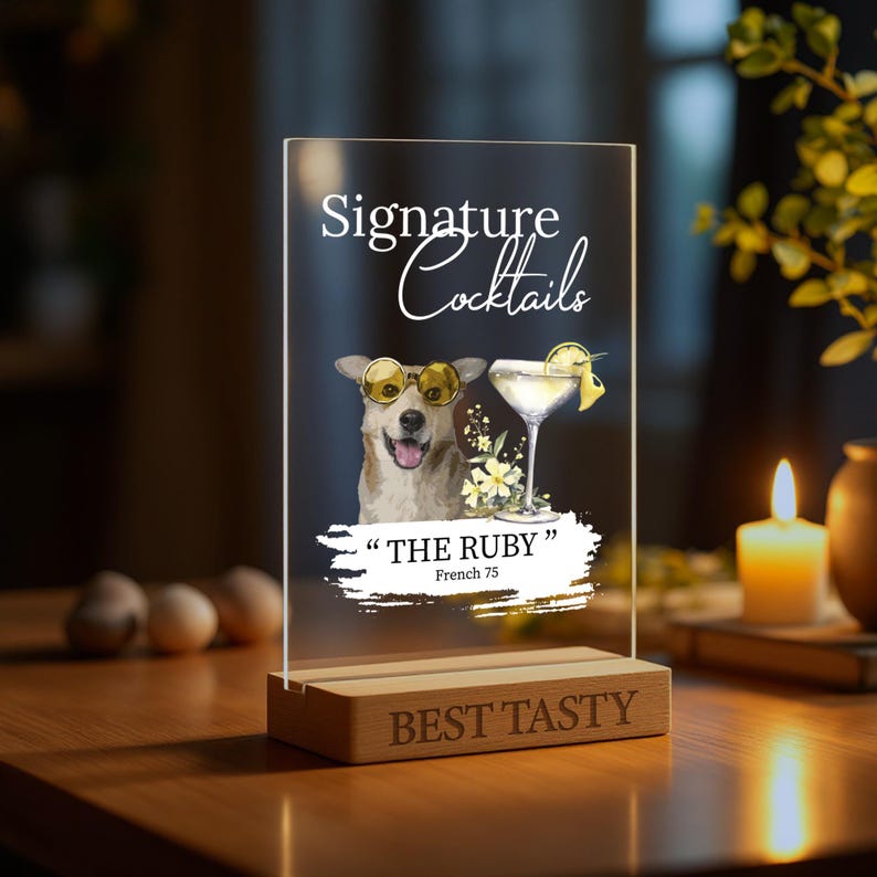 May include: A clear acrylic sign with a cartoon dog wearing sunglasses and a cocktail glass. The sign reads "Signature Cocktails" and "The Ruby" with the text "French 75" underneath. The sign is on a wooden base with the text "Best Tasty" engraved on it.