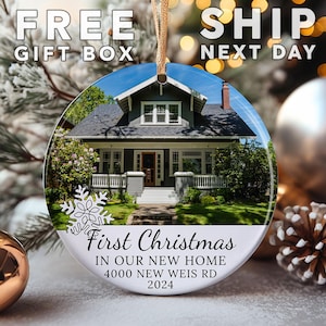 May include: Round Christmas ornament featuring a house with a gray exterior and white trim. The ornament has the text "First Christmas In Our New Home 4000 NEW WEIS RD 2024". A gold string is attached for hanging. The words "FREE GIFT BOX" and "SHIP NEXT DAY" are also visible.