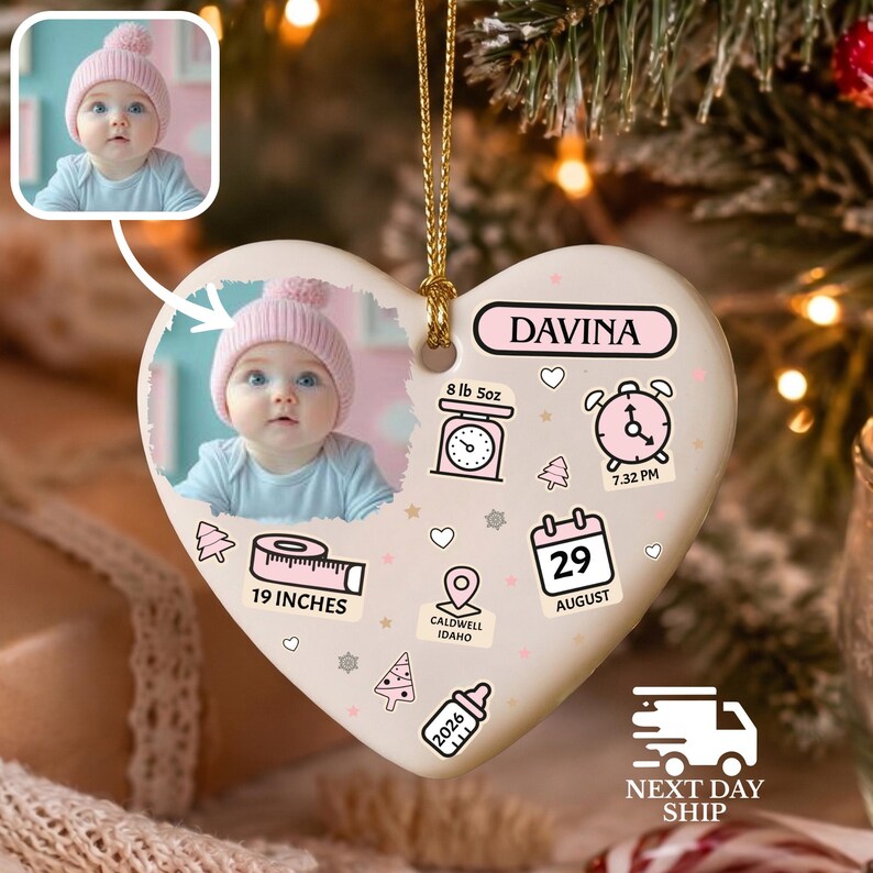 K&ouml;nnte beinhalten: Ein herzf&ouml;rmiger Keramikschmuck mit einem Foto eines Babys in einer rosa M&uuml;tze, dem Namen DAVINA und Geburtsdaten wie 8 lb 5oz, 19:32 Uhr, 19 inches, 29. August, Caldwell Idaho und 2026, verziert mit rosa Symbolen einer Waage, Uhr und Flasche.