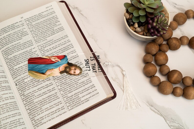 May include: A clear acrylic bookmark with a picture of Jesus Christ and the text "Micheal! Is that SMUT?" printed on it. The bookmark has a white tassel.