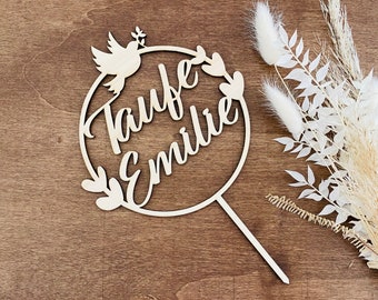 May include: Wooden cake topper with a circular design, featuring a dove with an olive branch, the words "Taufe Emilie" and floral accents.