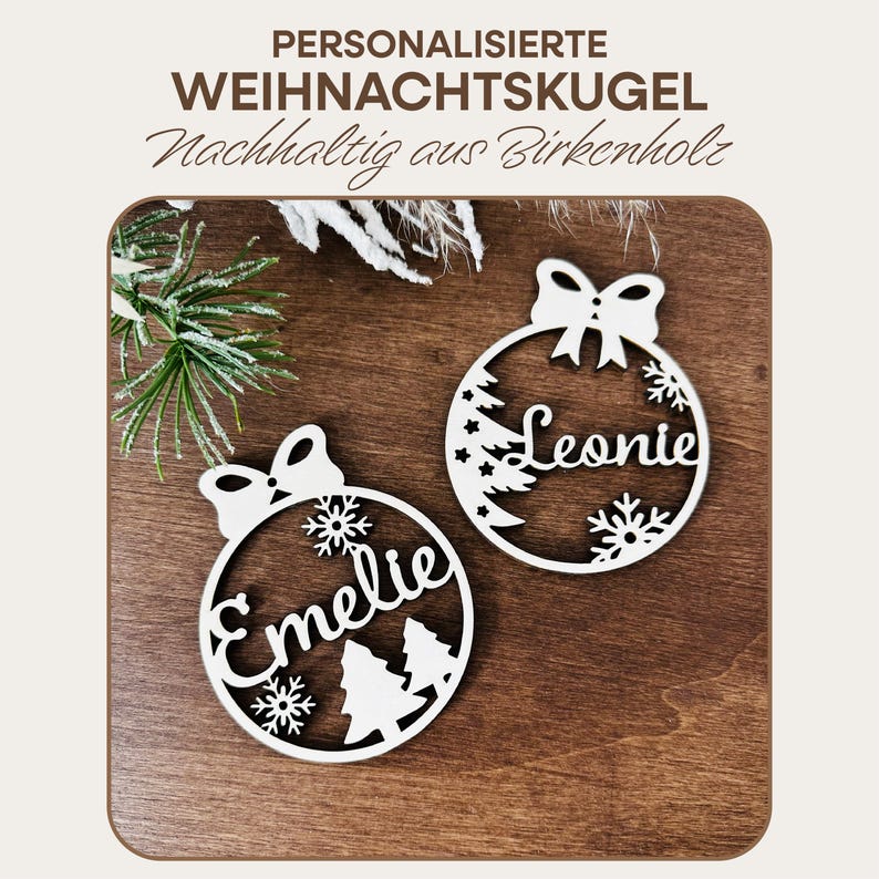 May include: Two white wooden Christmas ornaments with a bow and snowflakes. The ornaments are personalized with the names "Leonie" and "Emellie".
