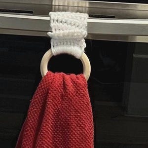 May include: White crocheted towel ring with a wooden ring and a red towel hanging from it.