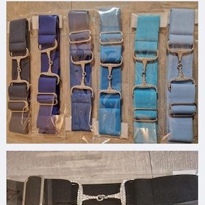 Op de afbeelding: Een collectie elastische riemen in diverse effen kleuren, elk voorzien van een centrale zilverkleurige metalen bitgesp versierd met heldere strass-steentjes. De riemen zijn individueel verpakt in doorzichtige plastic hoezen en bevatten verstelbare metalen schuifgespen.