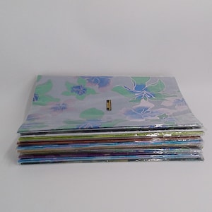 May include: A stack of floral-patterned fabric sheets in various colors. The top sheet features a light blue background with green and blue flower designs. The sheets are neatly stacked and wrapped in clear plastic.