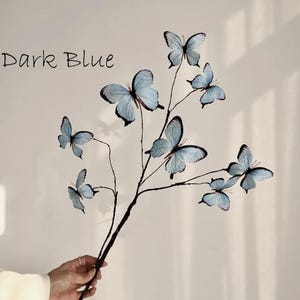 May include: A decorative branch featuring light blue butterflies with black detailing. The butterflies are attached to dark brown stems. The words "Dark Blue" are written in black script in the upper left corner.