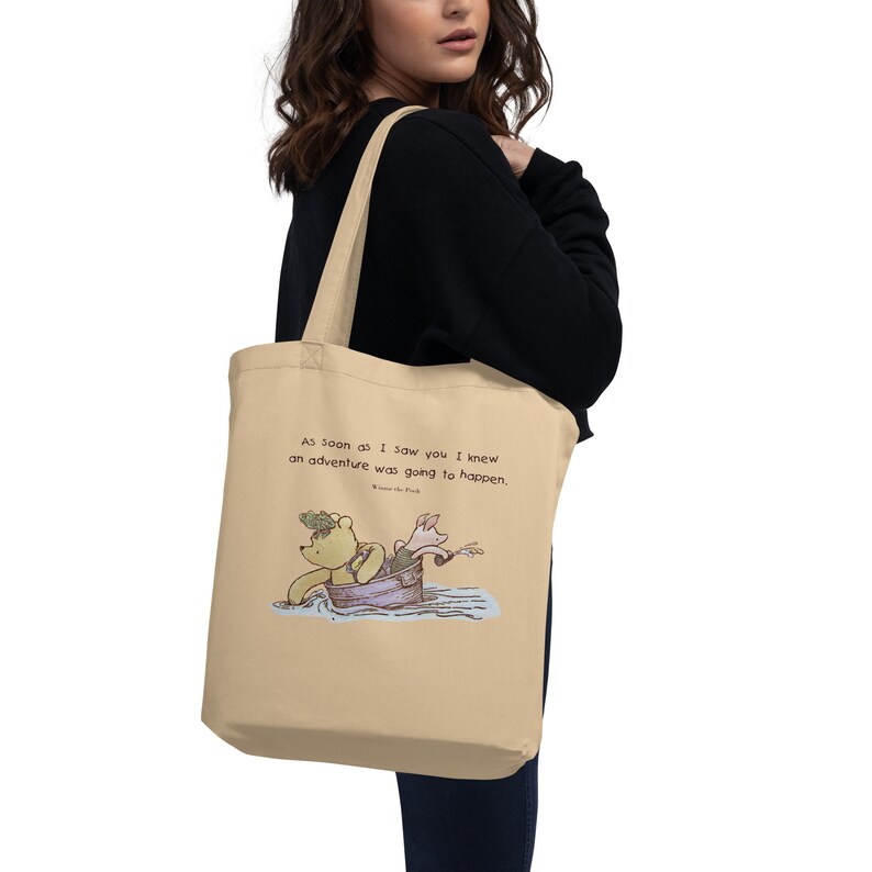 May include: A beige canvas tote bag with a Winnie the Pooh and Piglet illustration. The bag has a quote that reads "As soon as I saw you I knew an adventure was going to happen."