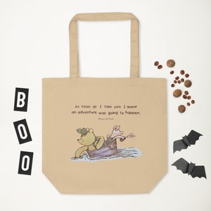 May include: A beige tote bag with a quote from Winnie the Pooh: "As soon as I saw you I knew an adventure was going to happen." The quote is in brown text and the image of Winnie the Pooh and Piglet in a boat is in the center of the bag.