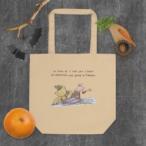 May include: A beige tote bag with a Winnie the Pooh and Piglet illustration. The text on the bag reads "As soon as I saw you I knew an adventure was going to happen."