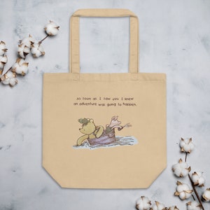 May include: A beige tote bag with a Winnie the Pooh and Piglet illustration. The text on the bag reads "As soon as I saw you I knew an adventure was going to happen."