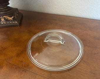 This is a vintage Pyrex L-21-C clear glass replacement lid featuring a distinctive arched "half-moon" or "fin" handle.