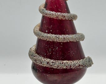 A blown glass Christmas tree figurine or tabletop sculpture, often featuring hand-applied silver or white "snow" or garland.