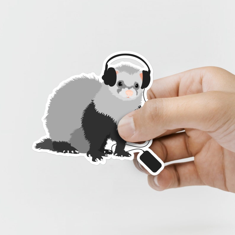 Hand holding funny sticker with a cute ferret wearing headphones and listening to music