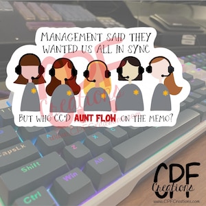 May include: A sticker featuring five cartoon figures wearing headsets, with the text "MANAGEMENT SAID THEY WANTED US ALL IN SYNC BUT WHO CC'D AUNT FLOW ON THE MEMO?" The sticker is on a keyboard.