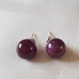 May include: A pair of silver stud earrings with round, dark purple gemstones.