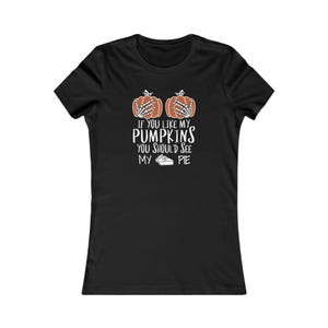 May include: A black short-sleeve t-shirt featuring a graphic of two orange pumpkins with white skeleton hands placed over them. Below the pumpkins, the white text reads: IF YOU LIKE MY PUMPKINS YOU SHOULD SEE MY PIE, accompanied by a small pie icon.