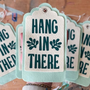 K&ouml;nnte beinhalten: Ein Set aus drei gr&uuml;nen und wei&szlig;en Filz-Geschenk-Etiketten mit dem Text "Hang in there" und einem Blatt-Design.