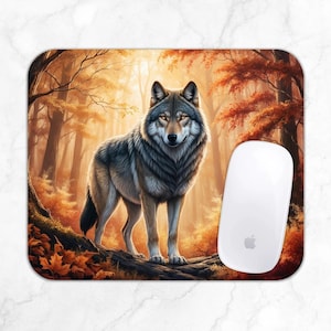 May include: Rectangular mousepad featuring a detailed illustration of a gray wolf standing in an autumn forest. The background shows trees with orange and red leaves. A white computer mouse is on the right side of the mousepad.