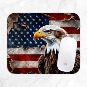 May include: Rectangular mousepad featuring a detailed illustration of an American bald eagle with a yellow beak and piercing blue eyes. The background shows a distressed American flag with red and white stripes and blue stars. A white computer mouse is on the right.
