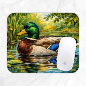 Op de afbeelding: Een rechthoekige muismat met een levendig olieverfschilderij van een wilde eend die in een vijver zwemt. De eend heeft een groene kop, een gele snavel en bruine en witte veren. Een witte computermuis rust aan de rechterkant van de muismat.