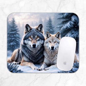 May include: A rectangular mousepad featuring a winter scene with two wolves lying in the snow. The wolves have gray and tan fur with yellow eyes. A white computer mouse is on the right side of the mousepad. The background shows snow-covered pine trees.