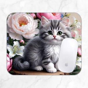May include: A gray and white kitten with green eyes sits in a bed of pink and white flowers. The kitten is looking directly at the camera. A white computer mouse is to the right of the kitten.