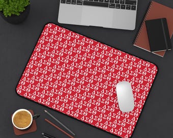 May include: A red mousepad with a repeating white pattern of Greek letters, including Delta, Sigma, and Theta. A white computer mouse sits on the pad, with a laptop, notebook, and coffee cup in the background.