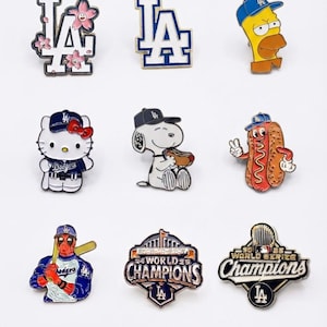 May include: A collection of nine enamel pins featuring Los Angeles Dodgers themes, including the LA logo with cherry blossoms, Homer Simpson, Hello Kitty, Snoopy with a hot dog, a hot dog character, Deadpool, and two World Series Champions designs.