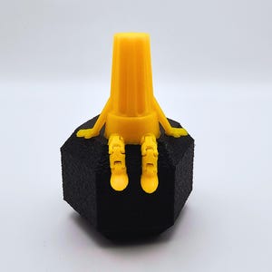 May include: A yellow 3D printed figurine of a person sitting on a black octagonal base. The figurine has a cylindrical body and segmented arms and legs.