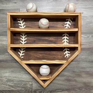 May include: A wooden baseball diamond-shaped shelf with three shelves and a bottom shelf with holes for displaying baseballs. Four baseballs are displayed on the shelves.