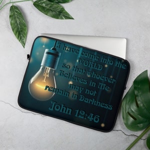 Puede incluir: Una funda para portátil negra con un fondo azul claro y una bombilla incandescente. El texto "Yo he venido al MUNDO para que todo aquel que cree en mí no permanezca en tinieblas Juan 12:46" está impreso en la funda.