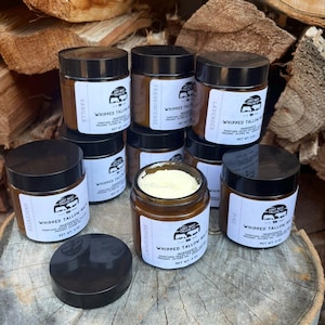 May include: An assortment of glass jars with black lids, labeled with various scents like vanilla, frankincense, and lavender. The jars are filled with a creamy, white substance and are arranged on a wooden surface. Each jar is 4 oz.