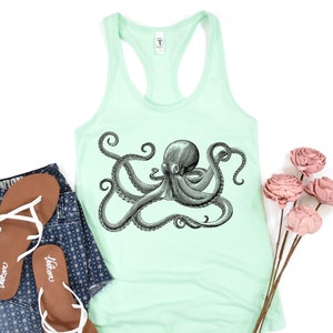 May include: A mint green tank top with a black and white illustration of an octopus on the front. The tank top is paired with denim shorts and brown sandals.