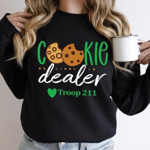 May include: Black sweatshirt with a green and white graphic that says "Cookie dealer" with two cookie images and a green heart with the text "Troop 211" underneath.