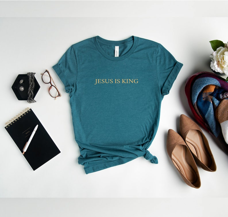 Pu&ograve; includere: Maglietta blu turchese con il testo "JESUS IS KING" in lettere dorate.
