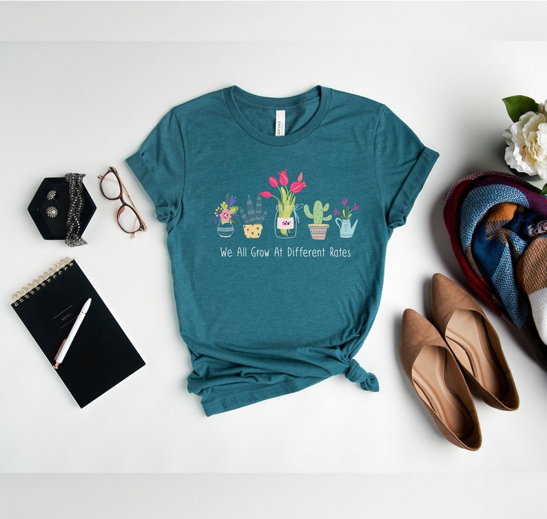 May include: Teal blue t-shirt with a graphic of potted plants and the text "We All Grow At Different Rates".