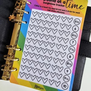 May include: A weight loss tracker card with a rainbow gradient border. The card features a grid of hearts and circles for tracking weight loss milestones. Text on the card reads "one pound at a time weightloss tracker".