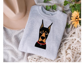 May include: A grey sweatshirt featuring an illustration of a black and brown Doberman Pinscher wearing a red collar.