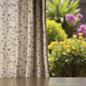 Könnte beinhalten: Beigefarbener Vorhang mit einem sich wiederholenden Blumenmuster in einem dunkleren Braunton. Der Vorhang ist teilweise geöffnet und gibt den Blick auf eine verschwommene Außenszene mit grünen und gelben Blättern und lila Blumen frei. Der Stoff des Vorhangs scheint leicht strukturiert zu sein.