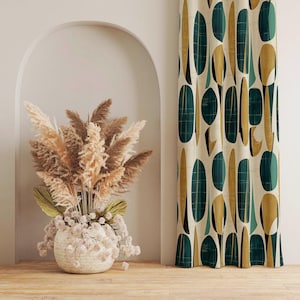 May include: An interior scene with a woven basket of dried pampas grass and a patterned curtain. The curtain has a cream background with teal and gold oval shapes. The basket sits on a wooden floor.