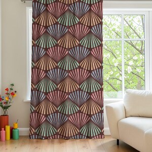 May include: A brown curtain with a repeating fan-shaped pattern in shades of pink, blue, green, and orange. The curtain hangs in front of a window, with a white couch visible in the background. The design is reminiscent of Art Deco.