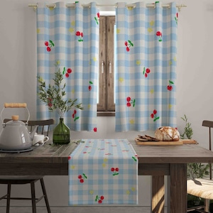 May include: A dining room scene featuring light blue and white checkered curtains with cherry and yellow flower patterns. A matching table runner is on a wooden table. A green vase with greenery and a teapot are also visible.