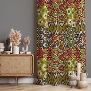 以下が含まれることがあります： パッチワークデザインのカラフルな柄のカーテン。カーテンは、緑、オレンジ、青、白の花柄と幾何学模様を組み合わせています。カーテンは灰色の壁の前に吊るされています。