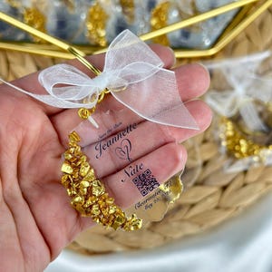 May include: Save the Date for Jeanette and Nate's wedding in Clearwater, FL on May 20, 2026. The invitation is a clear plastic card with gold glitter and a QR code.
