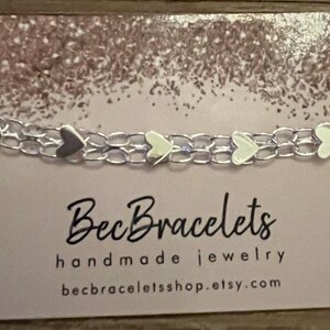 May include: A silver chain bracelet with small silver heart charms. The bracelet is displayed on a card with the text "BecBracelets handmade jewellery becbraceletshop.etsy.com".