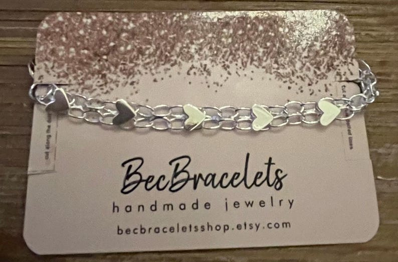May include: A silver chain bracelet with small silver heart charms. The bracelet is displayed on a card with the text "BecBracelets handmade jewellery becbraceletshop.etsy.com".